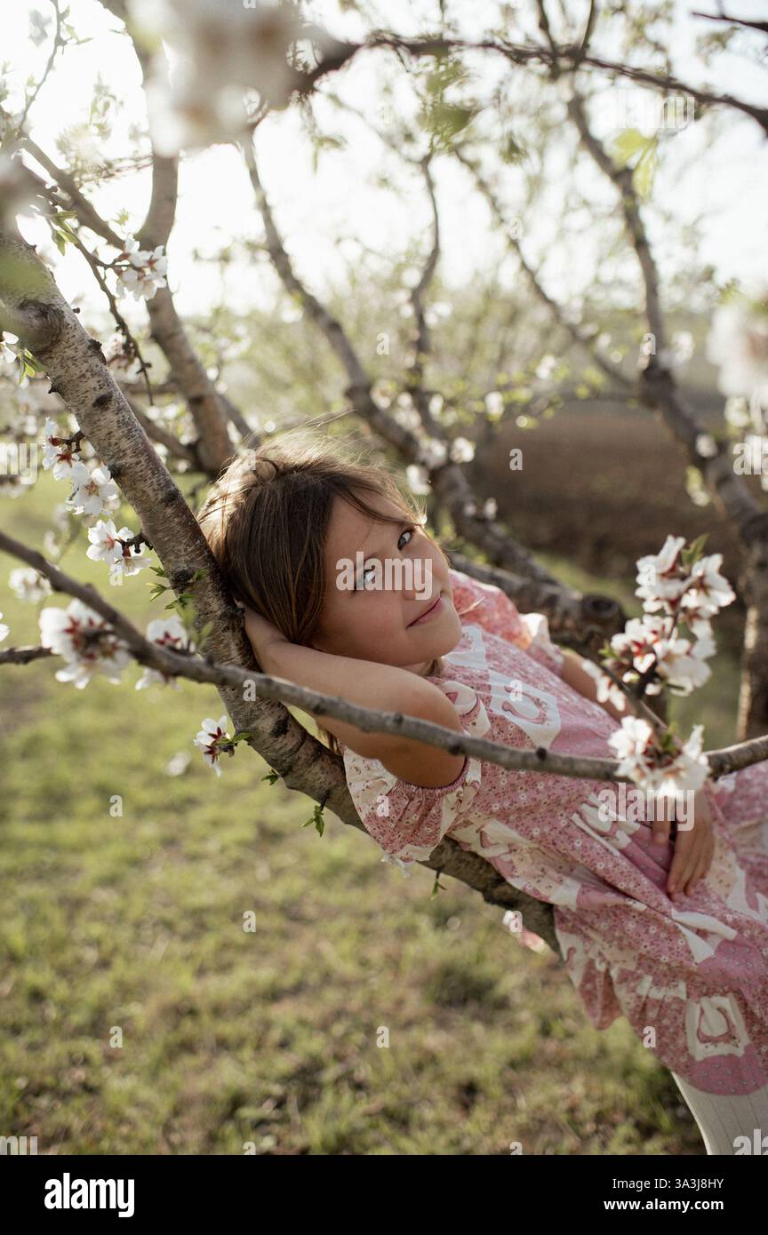 Ein fröhliches Mädchen spielt zwischen blühenden Mandelbäumen, ihr Lachen erfüllt die Frühlingsluft. Stockfoto