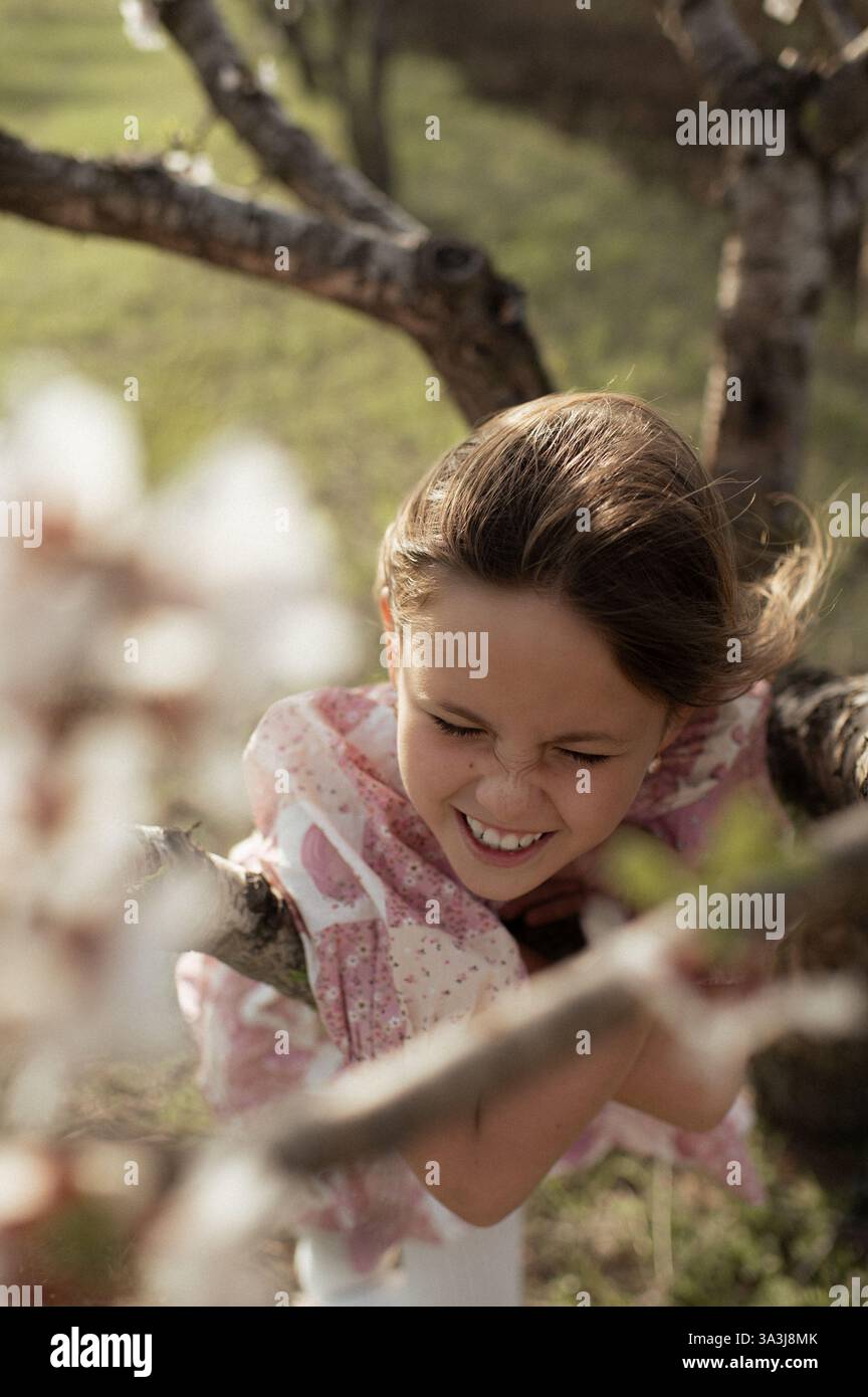 Ein fröhliches Mädchen spielt zwischen blühenden Mandelbäumen, ihr Lachen erfüllt die Frühlingsluft. Stockfoto