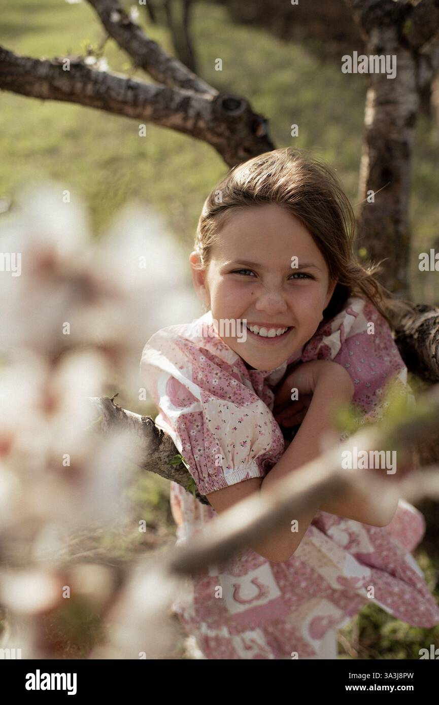Ein fröhliches Mädchen spielt zwischen blühenden Mandelbäumen, ihr Lachen erfüllt die Frühlingsluft. Stockfoto