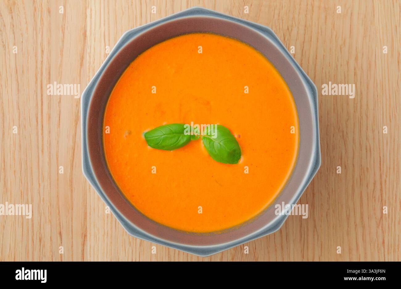 Eine Schüssel Suppe mit einem Basilikumblatt darauf. Die Schüssel steht auf einem Holztisch Stockfoto