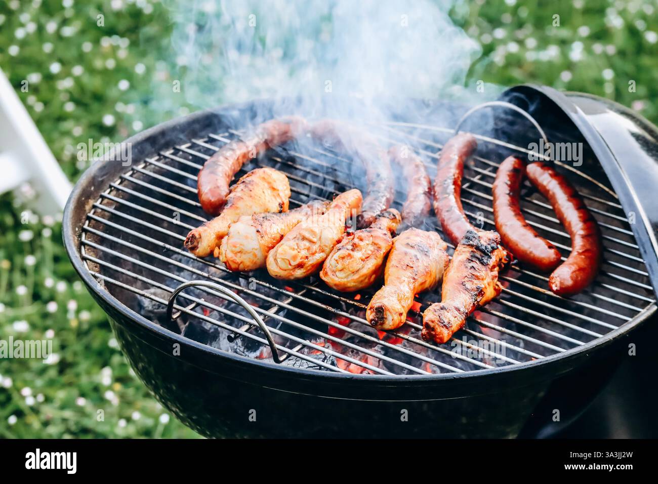 Hähnchenschenkel und Merguez-Würstchen, die auf einem Grill im Garten zubereitet werden Stockfoto