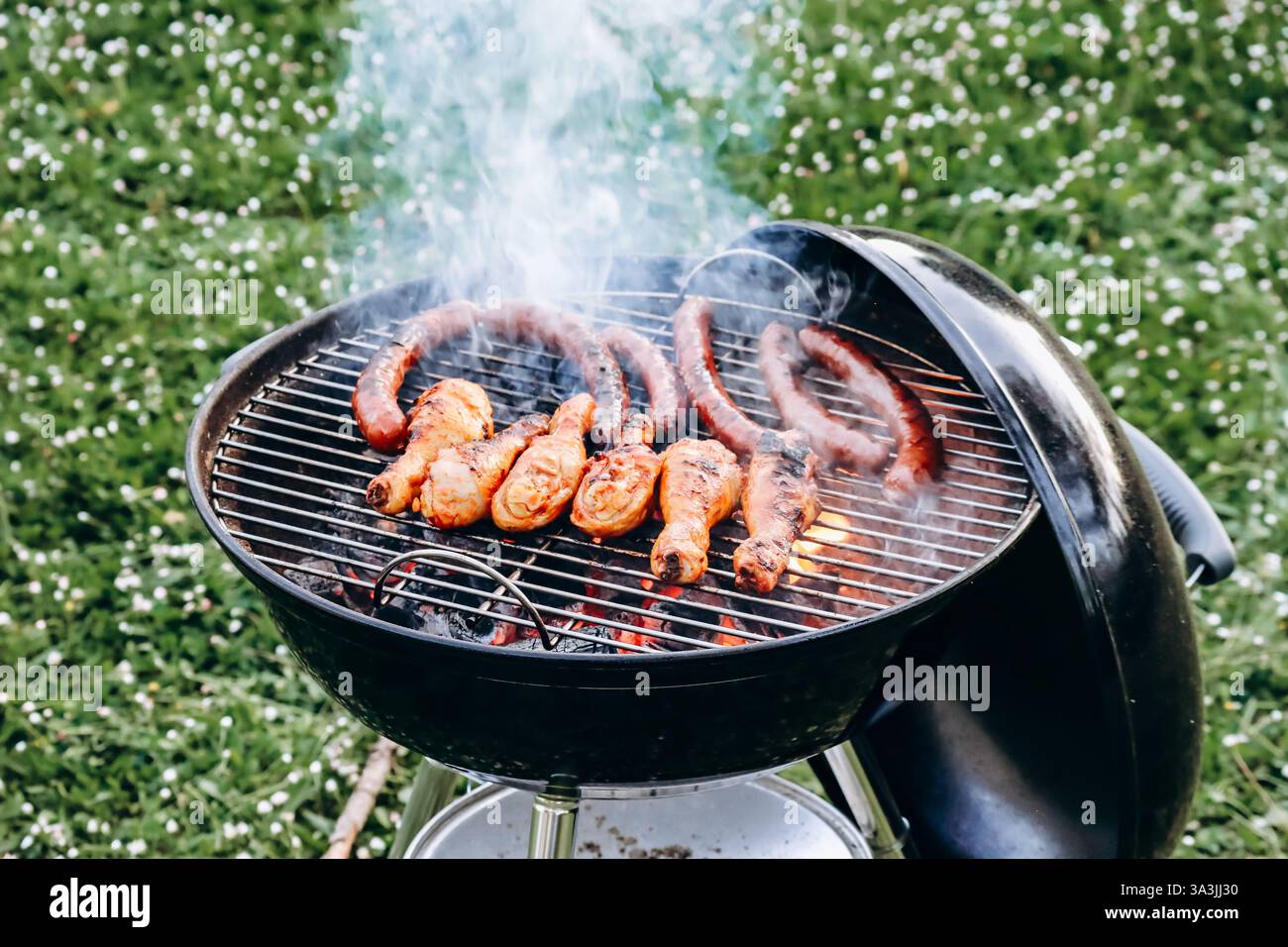 Hähnchenschenkel und Merguez-Würstchen, die auf einem Grill im Garten zubereitet werden Stockfoto