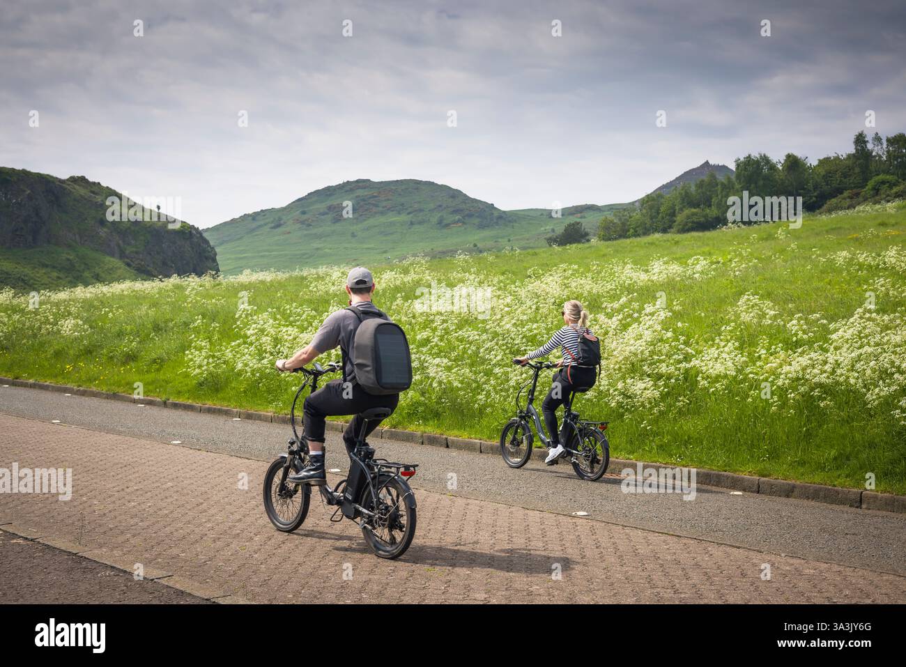 Edinburgh, Großbritannien - 31. Mai 2024. Zwei Touristen fahren mit dem Fahrrad durch den Holyrood Park mit Arthurs-Sitz im Hintergrund. Edinburgh, Schottland, Großbritannien Stockfoto