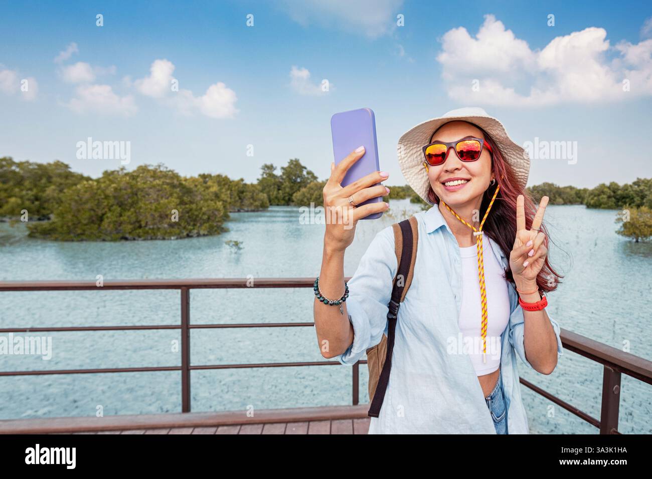 Weibliche Touristen, die ein Selfie auf einer hölzernen Promenade inmitten von Mangroven und türkisfarbenem Wasser im Mangrovenpark in Abu Dhabi machen Stockfoto