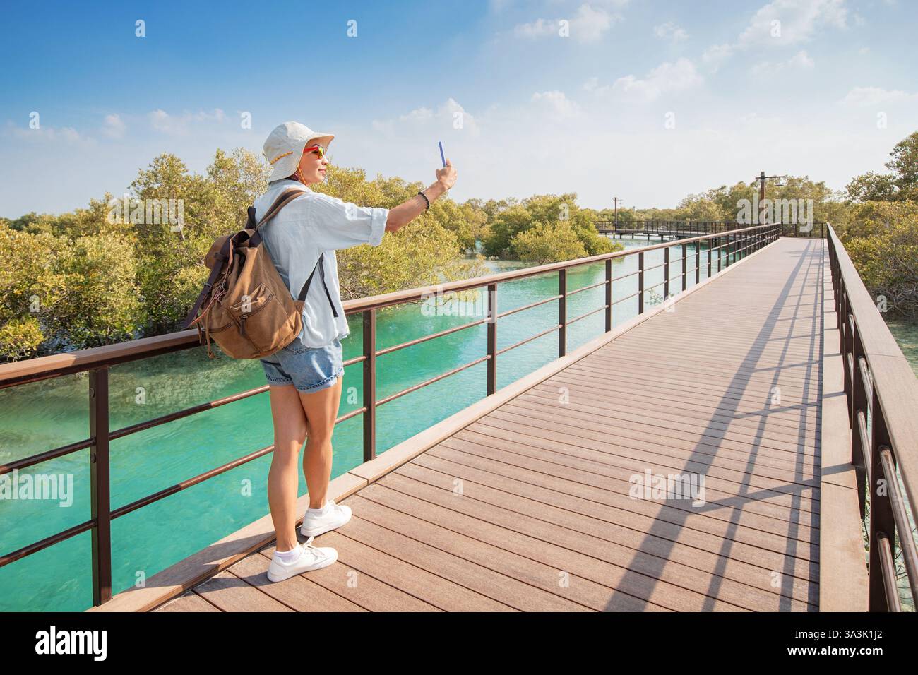 Weibliche Touristen, die ein Selfie auf einer hölzernen Promenade inmitten von Mangroven und türkisfarbenem Wasser im Mangrovenpark in Abu Dhabi machen Stockfoto