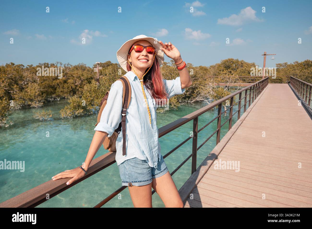 Frau genießt einen Spaziergang auf einer hölzernen Promenade, umgeben von üppigem Grün und klarem Wasser, unter einem hellblauen Himmel in einem Naturschutzgebiet Stockfoto