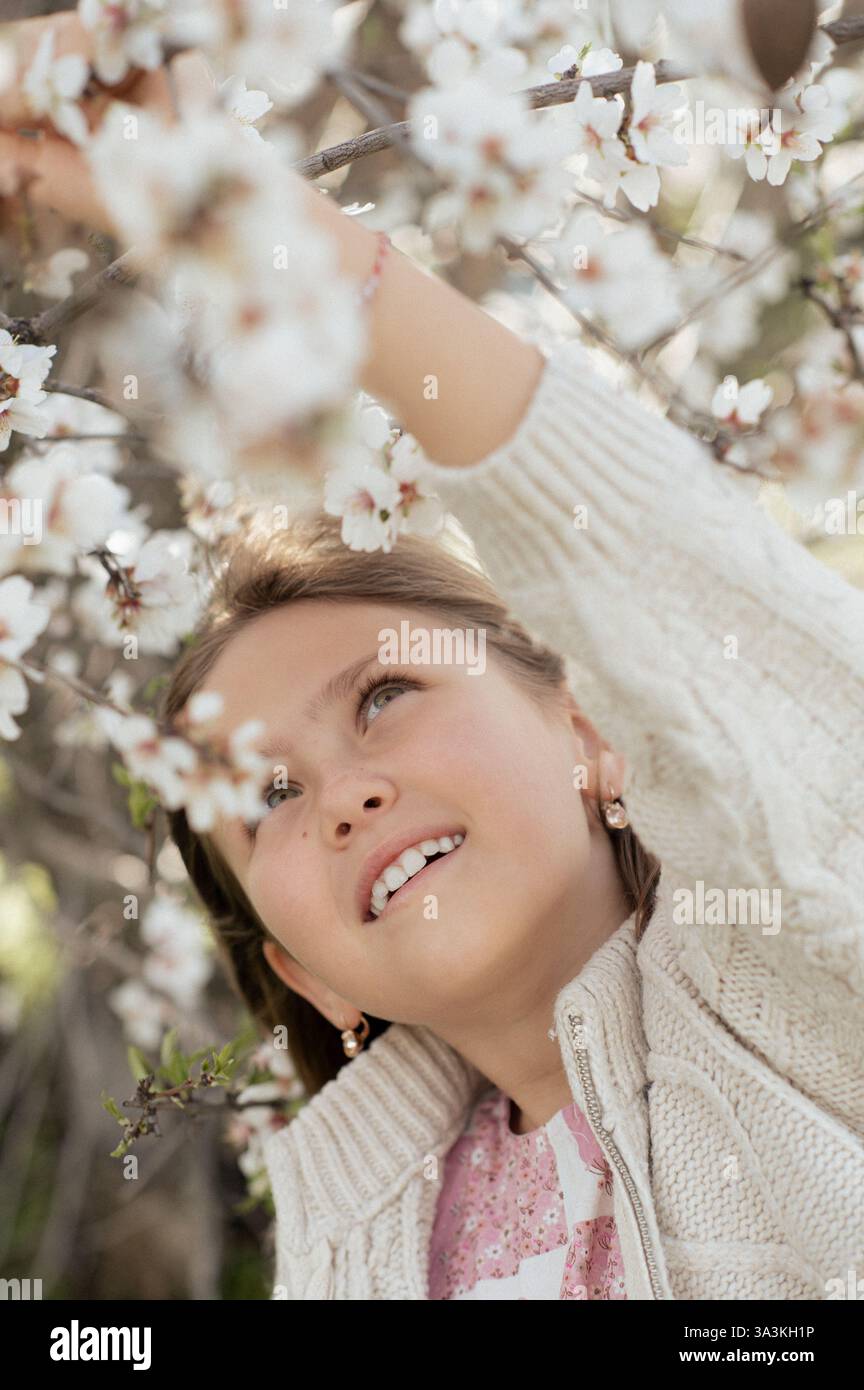 Ein Junge sitzt unter einem blühenden Mandelbaum, pflückt frische Mandeln und hält sie in seinen Händen. Stockfoto
