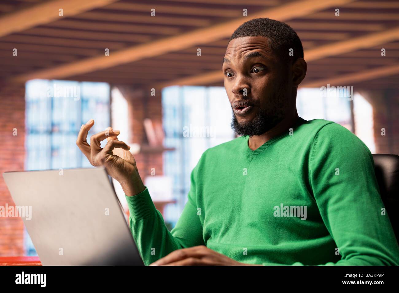 Ein Mann zu Hause, der eine Fernsehsendung auf einem Laptop ansieht, schockiert von einer interessanten Handlung. afroamerikaner, der Fernsehserien in der Wohnung genießt, überrascht von der fesselnden Wende der Ereignisse Stockfoto