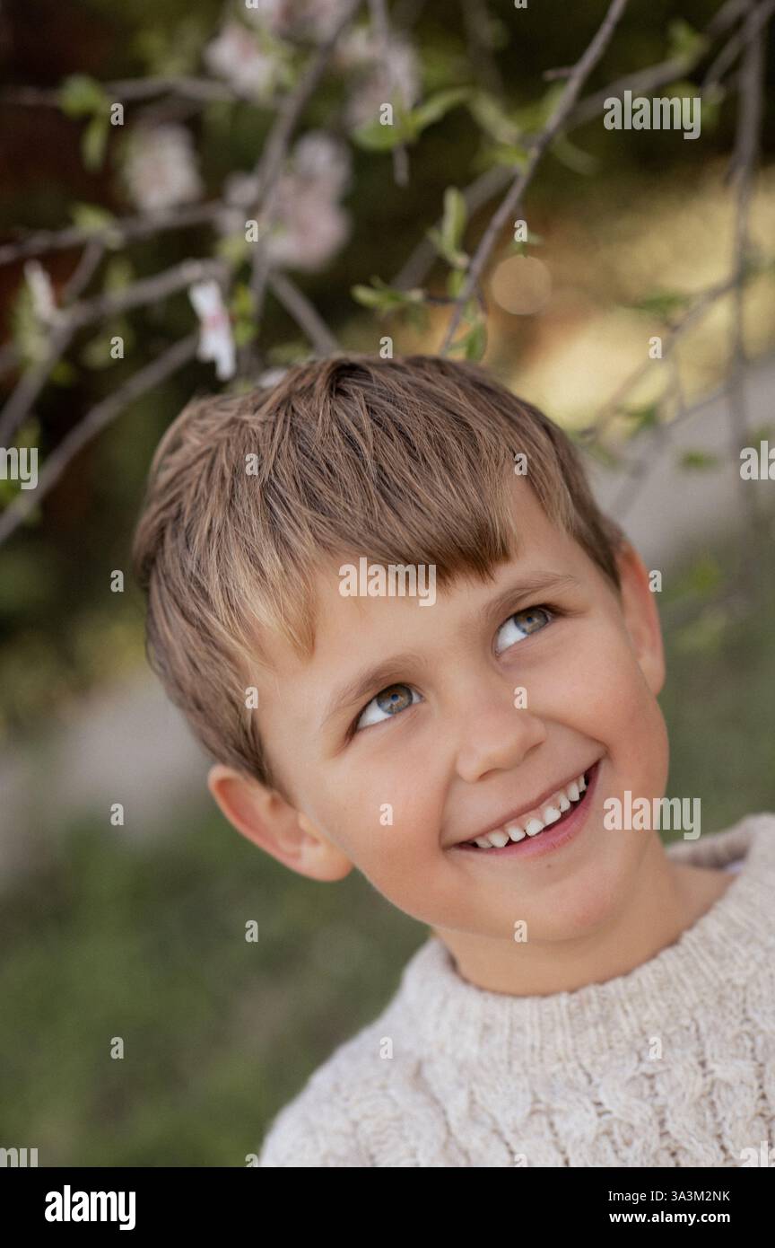 Ein Junge sitzt unter einem blühenden Mandelbaum, pflückt frische Mandeln und hält sie in seinen Händen. Stockfoto