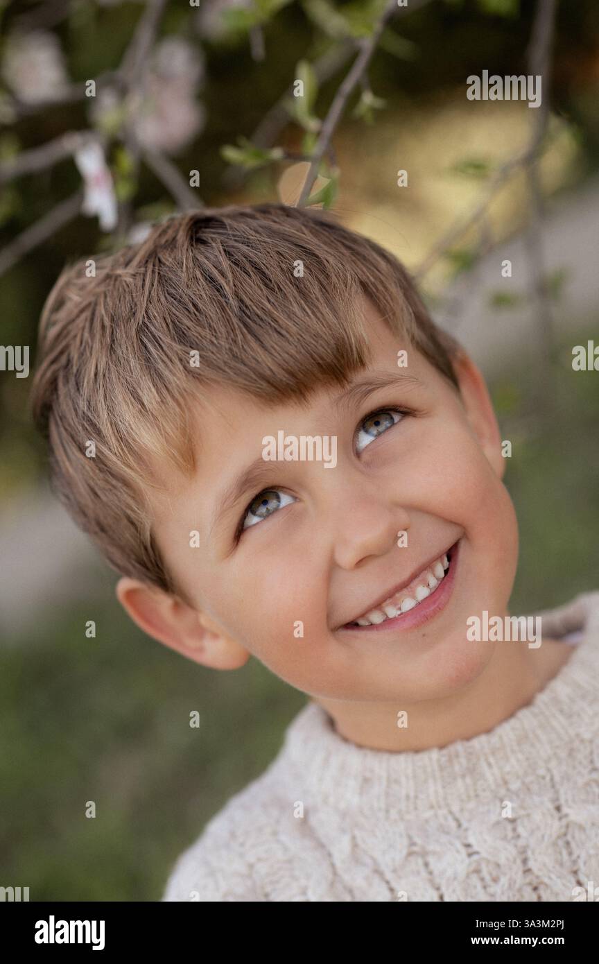 Ein Junge sitzt unter einem blühenden Mandelbaum, pflückt frische Mandeln und hält sie in seinen Händen. Stockfoto