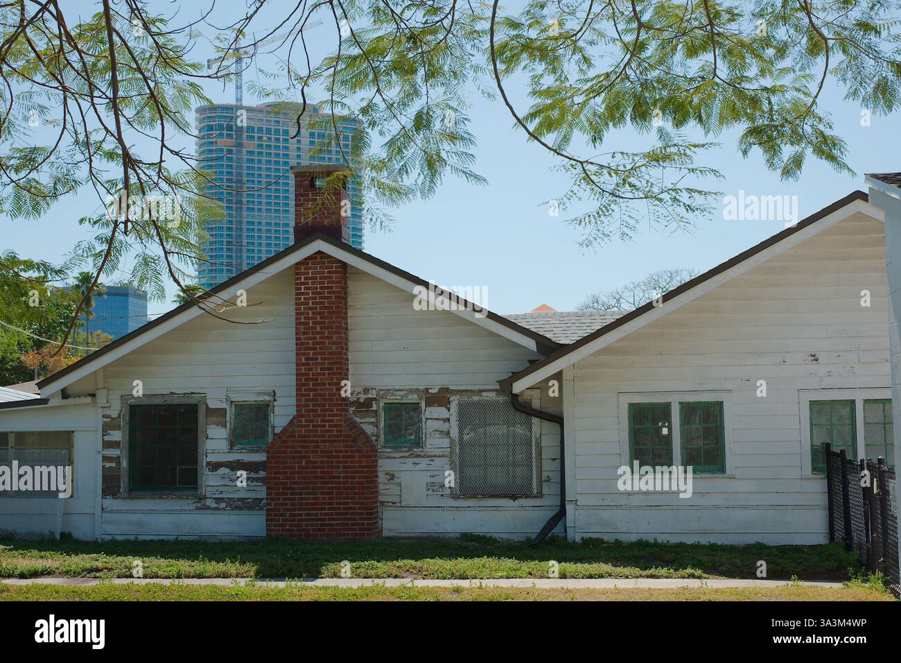 Altes, leicht verwittertes weißes einstöckiges Gebäude mit rotem Backsteinkamin, zentral gelegen vor dem Hintergrund eines hohen modernen Hochhauses Stockfoto