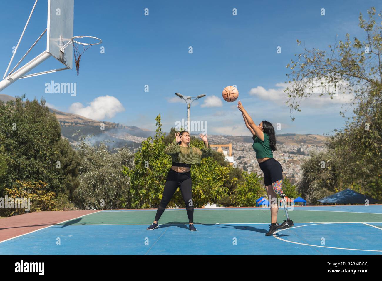 Zwei junge Frauen spielen Basketball auf einem Freiluftplatz und zeigen Vielfalt, Inklusion und Leichtathletik Stockfoto