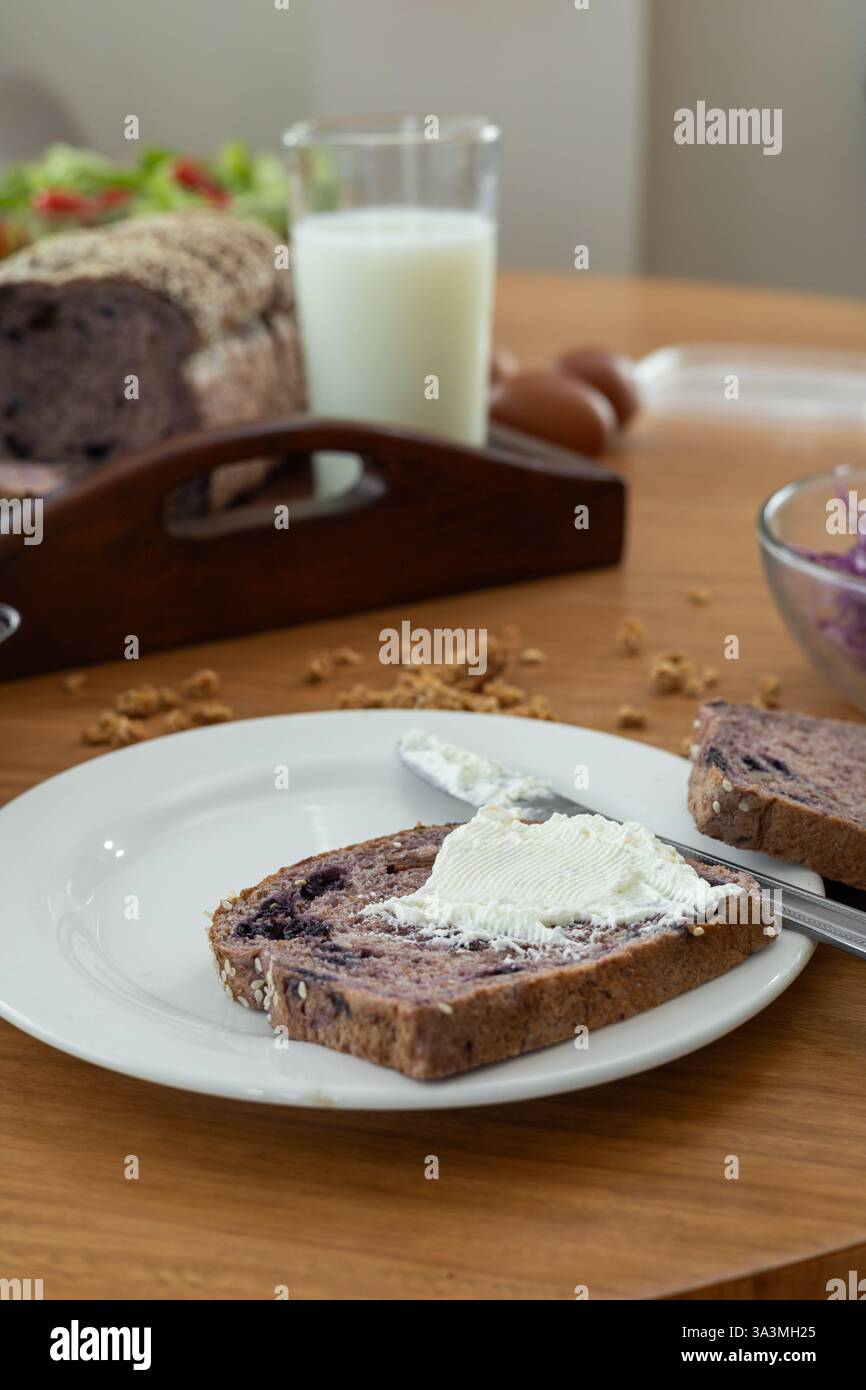 Ein zärtlicher Moment, während ein Messer liebevoll glatten Frischkäse auf eine weiche Brotscheibe verteilt und einen süßen und intimen Snack kreiert, der zum Wa einlädt Stockfoto