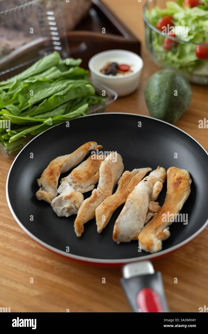 Goldbraune, knusprige, frittierte Hähnchenstreifen, die in einer gusseisernen Pfanne brutzeln, begleitet von einem erfrischenden Tomatensalat. Das dunkle Licht und die rustikale Atmosphäre von A c Stockfoto