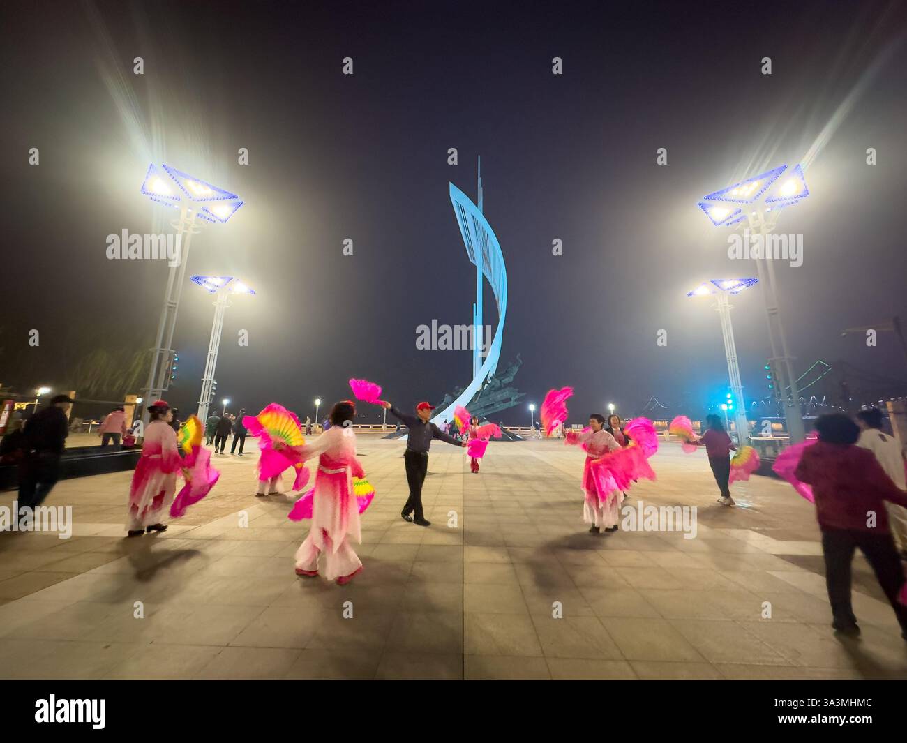 Die Menschen tanzen entlang der Promenade des Yalu-Flusses in traditioneller koreanischer Kleidung. Dandong bildet einen umstrittenen östlichen Endpunkt des Ming Great Wal Stockfoto