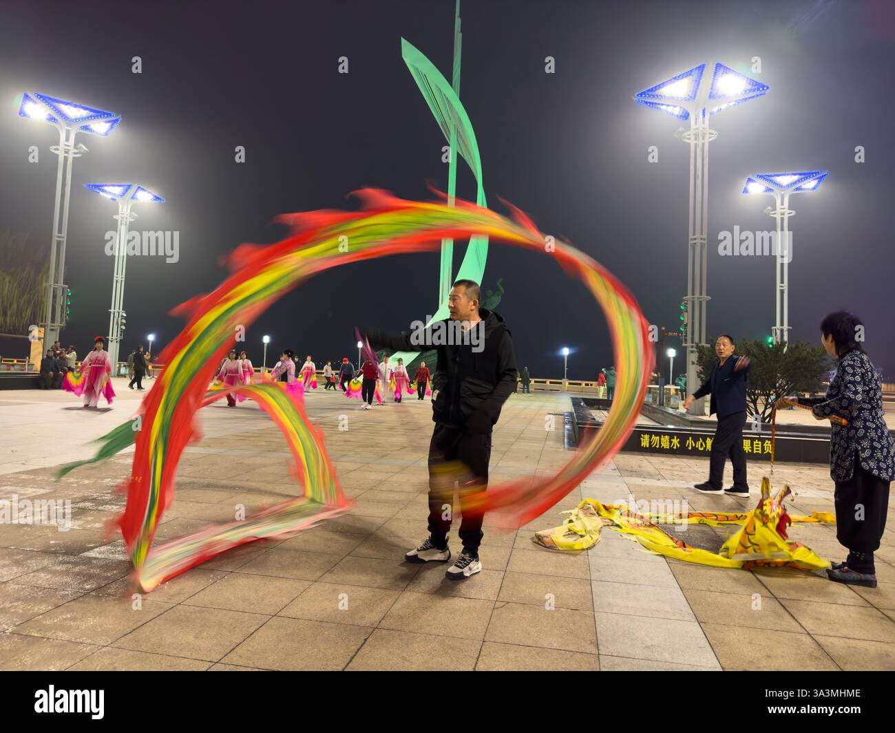 Die Menschen tanzen entlang der Promenade des Yalu-Flusses in traditioneller koreanischer Kleidung. Dandong bildet einen umstrittenen östlichen Endpunkt des Ming Great Wal Stockfoto