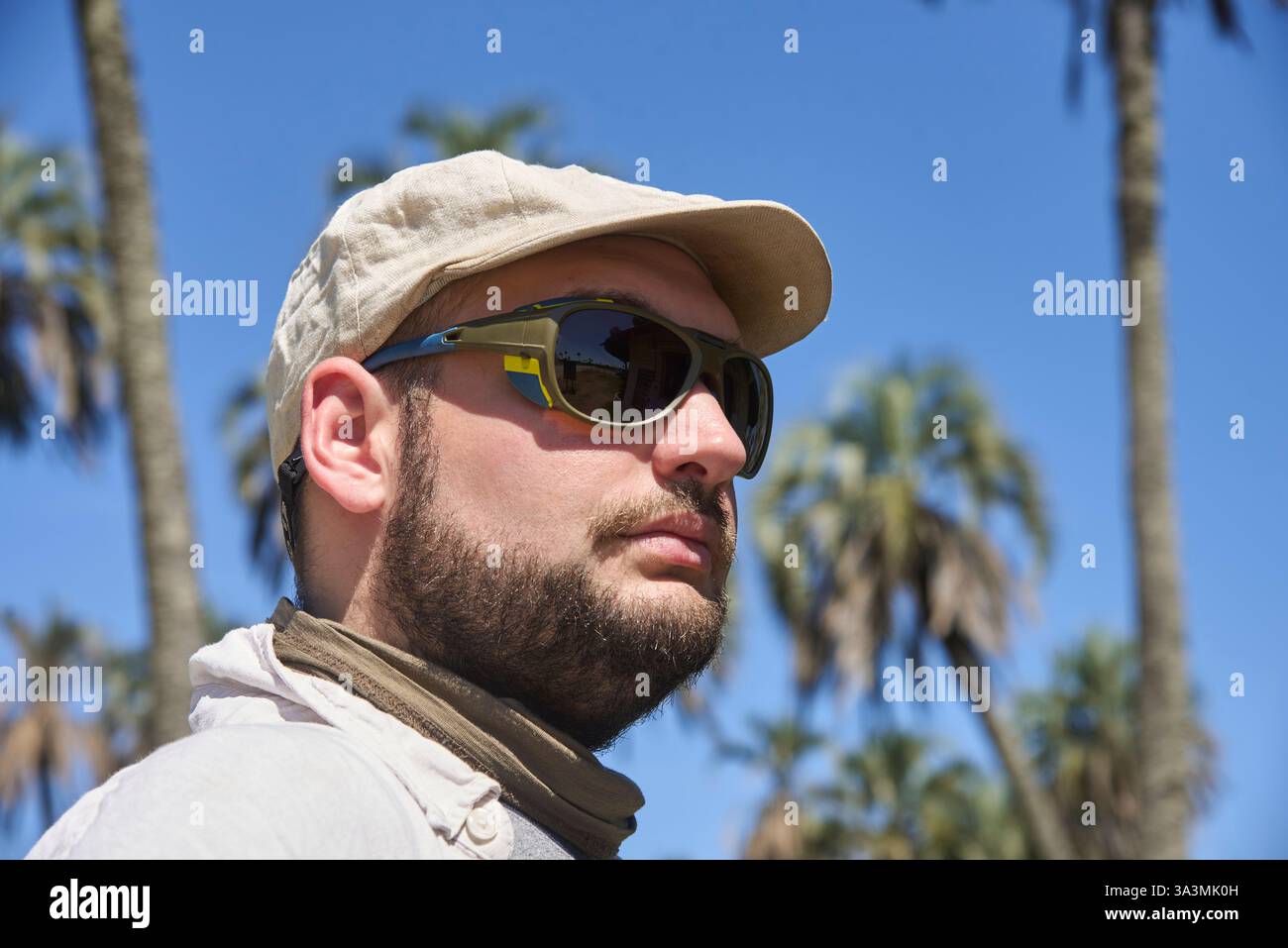 Porträt eines jungen Mannes mit Sonnenbrille und Leinenmütze draußen an einem sonnigen Tag, mit Palmen im Hintergrund. Reisende genießen die Natur in El PAL Stockfoto