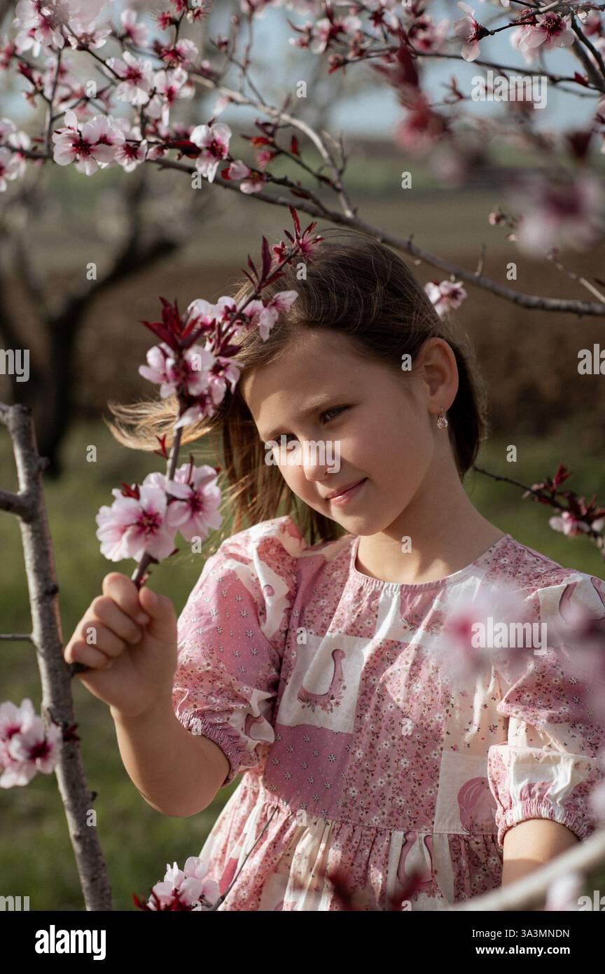 Ein fröhliches Mädchen spielt zwischen blühenden Mandelbäumen, ihr Lachen erfüllt die Frühlingsluft. Stockfoto