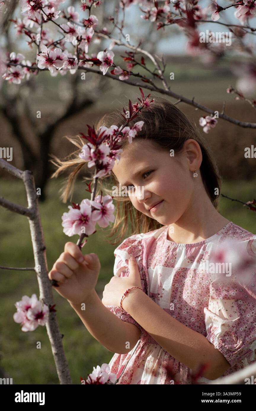 Ein fröhliches Mädchen spielt zwischen blühenden Mandelbäumen, ihr Lachen erfüllt die Frühlingsluft. Stockfoto