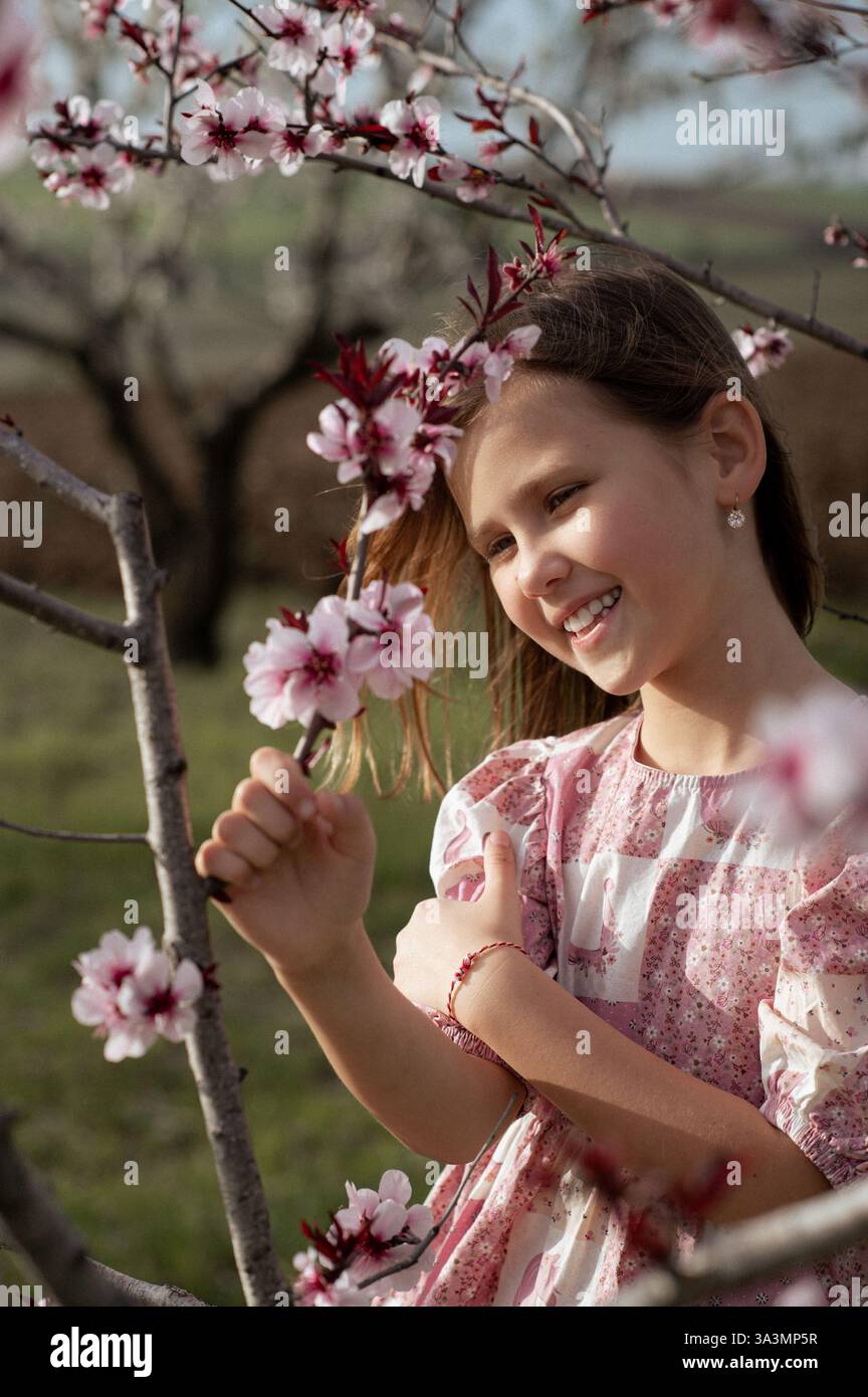 Ein fröhliches Mädchen spielt zwischen blühenden Mandelbäumen, ihr Lachen erfüllt die Frühlingsluft. Stockfoto
