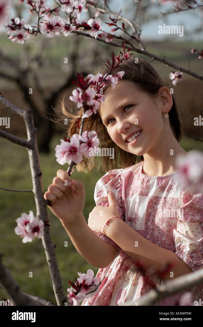 Ein fröhliches Mädchen spielt zwischen blühenden Mandelbäumen, ihr Lachen erfüllt die Frühlingsluft. Stockfoto