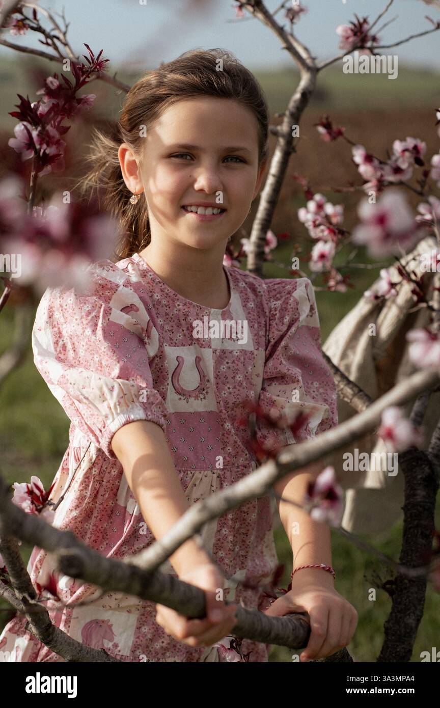Ein fröhliches Mädchen spielt zwischen blühenden Mandelbäumen, ihr Lachen erfüllt die Frühlingsluft. Stockfoto