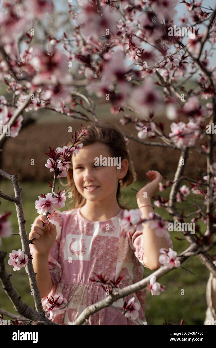 Ein fröhliches Mädchen spielt zwischen blühenden Mandelbäumen, ihr Lachen erfüllt die Frühlingsluft. Stockfoto