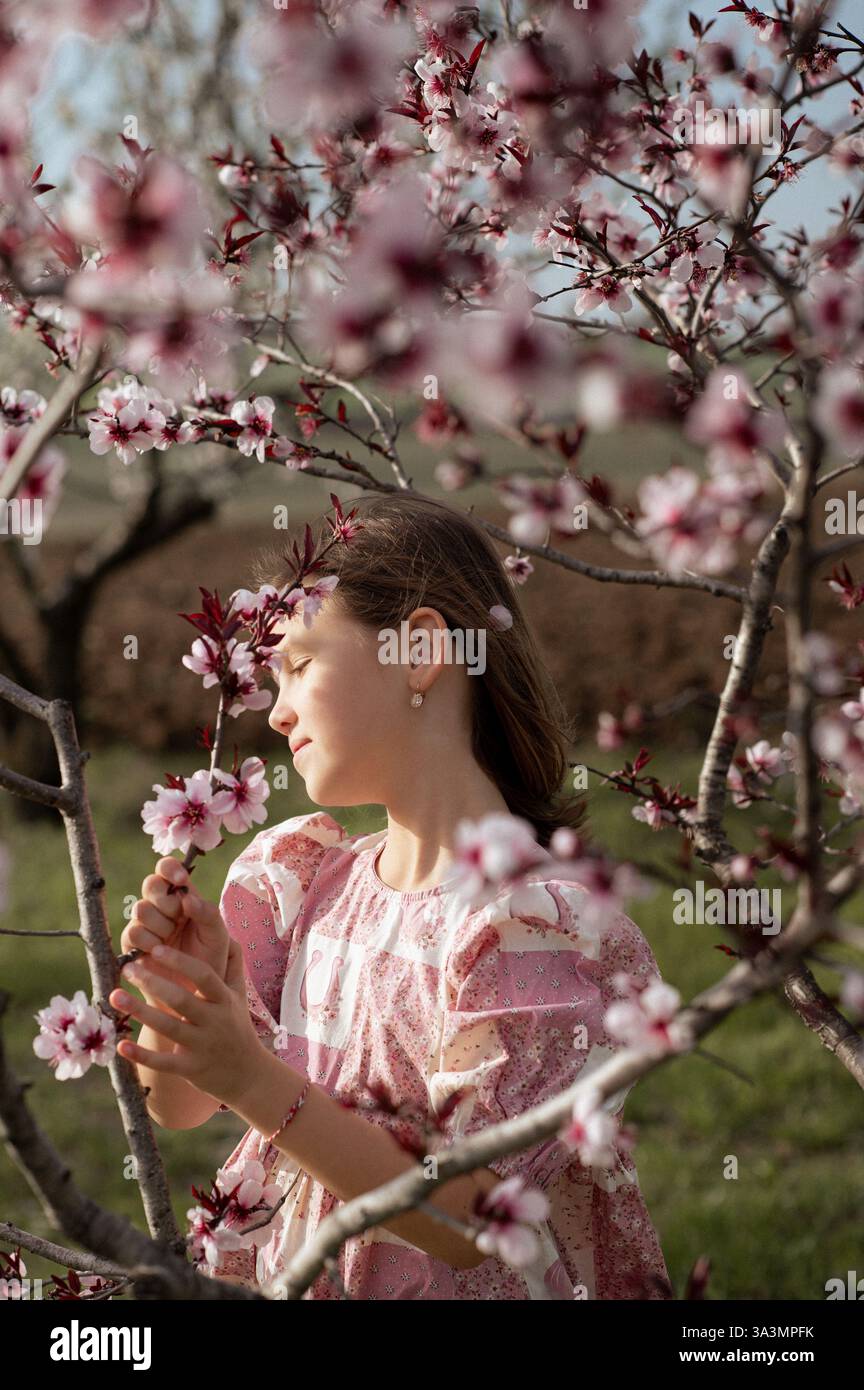 Ein fröhliches Mädchen spielt zwischen blühenden Mandelbäumen, ihr Lachen erfüllt die Frühlingsluft. Stockfoto