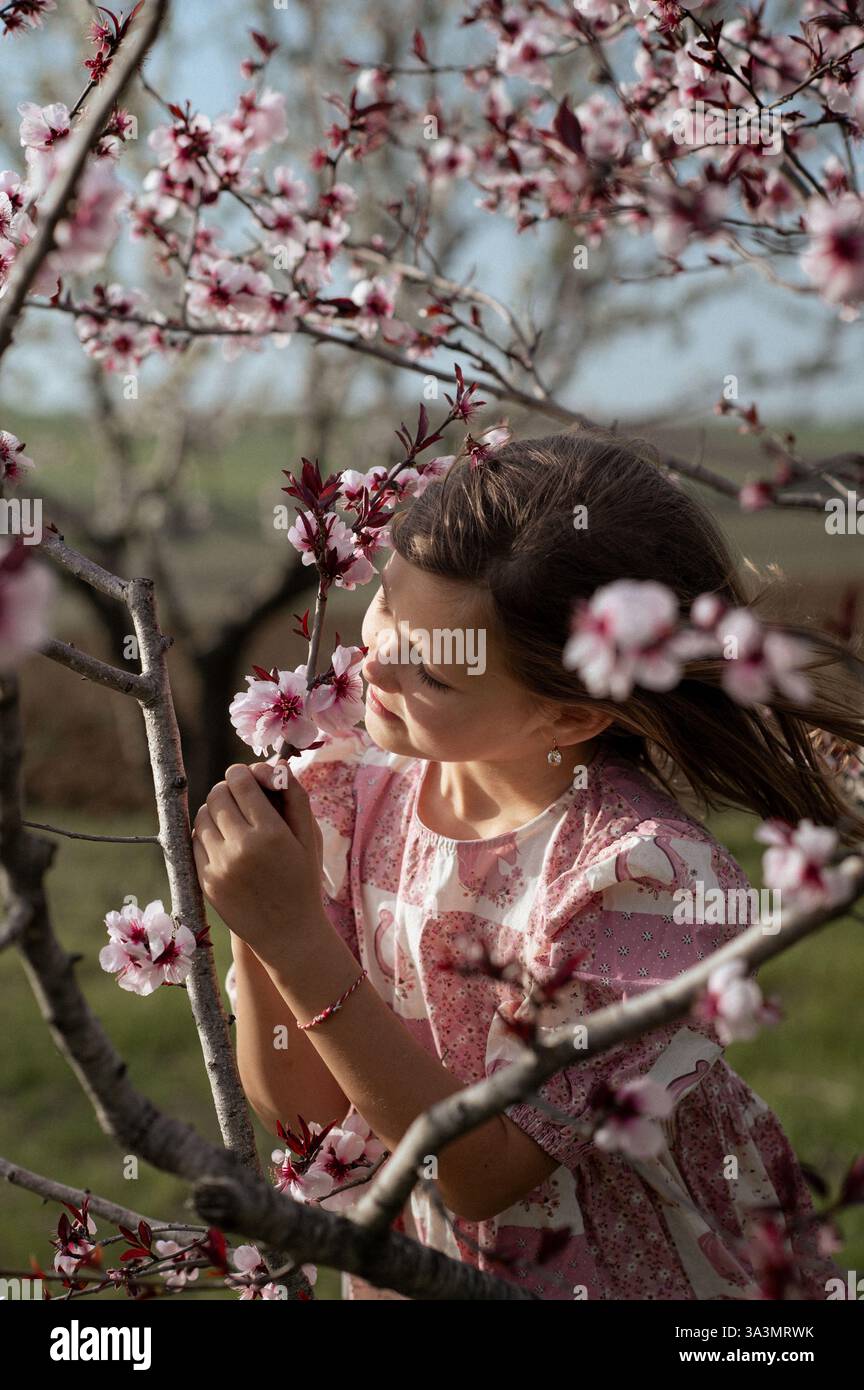 Ein fröhliches Mädchen spielt zwischen blühenden Mandelbäumen, ihr Lachen erfüllt die Frühlingsluft. Stockfoto