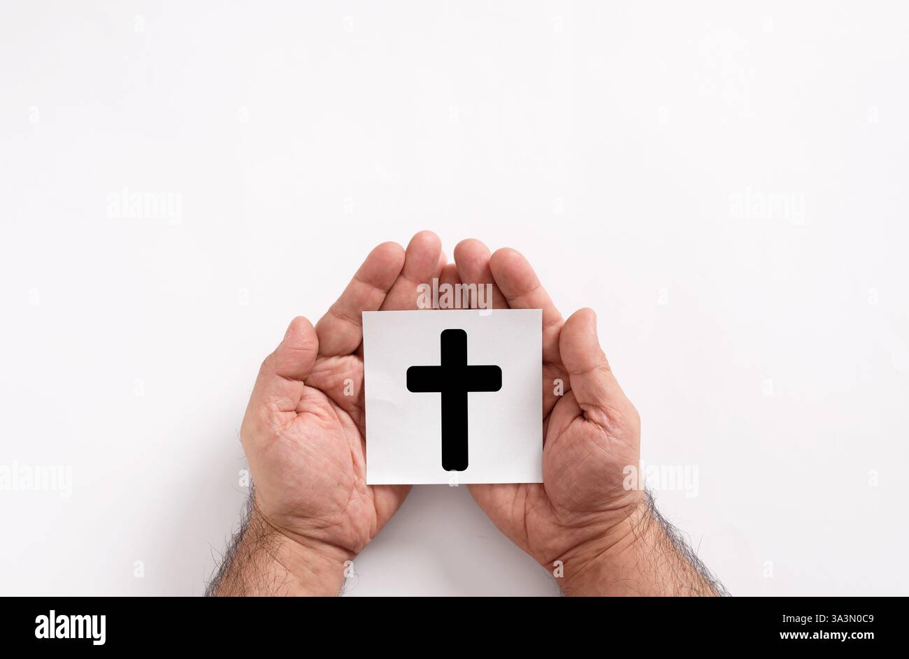Männliche Hände halten eine weiße Karte mit einem schwarzen Kreuz auf weißem Hintergrund, die Glauben, Hoffnung, Anbetung, Gebet und Christentum repräsentieren Stockfoto