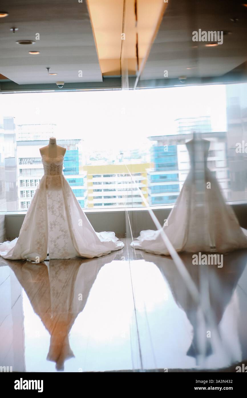 Zwei elegante Hochzeitskleider auf Schaufensterpuppen in einem modernen urbanen Ambiente. Das Bild weist Reflexionen auf dem glänzenden Boden auf, was die Verbesserung verbessert Stockfoto