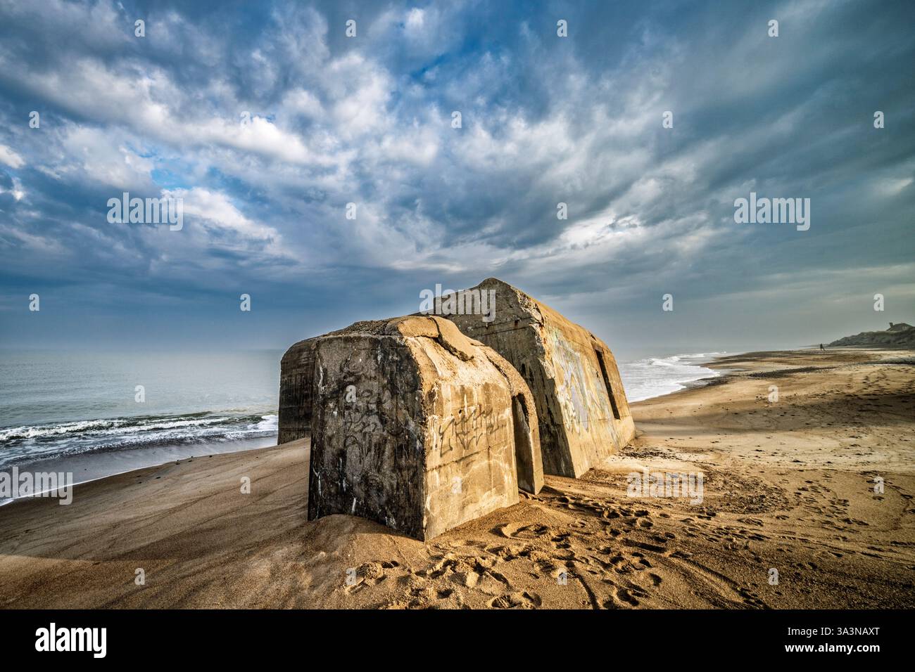 Ruhige Küstenszene mit großen Bunkern aus dem 2. weltkrieg mit verwitterten Strukturen unter einem stimmungsvoll bewölkten Himmel. Stockfoto