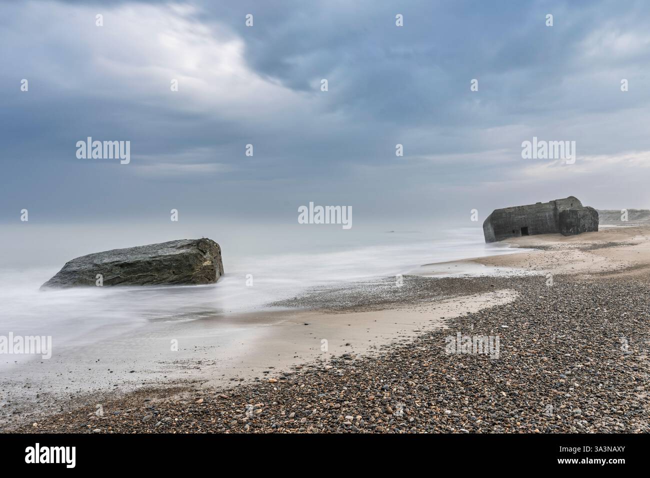 Ruhige Küstenszene mit großen Bunkern aus dem 2. weltkrieg mit verwitterten Strukturen unter einem stimmungsvoll bewölkten Himmel. Stockfoto