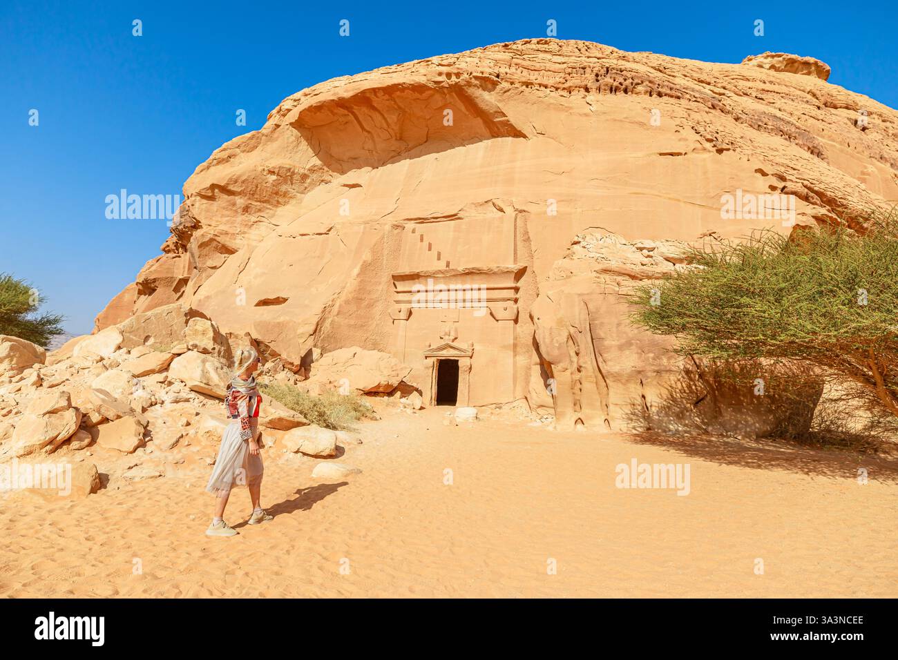 Blonde Touristen spazieren in der Wüste neben dem Jabal AlBanat und dem riesigen Felsengrab des nabatäischen Königreichs in der Hegra Archäologischen Stätte Madain Stockfoto