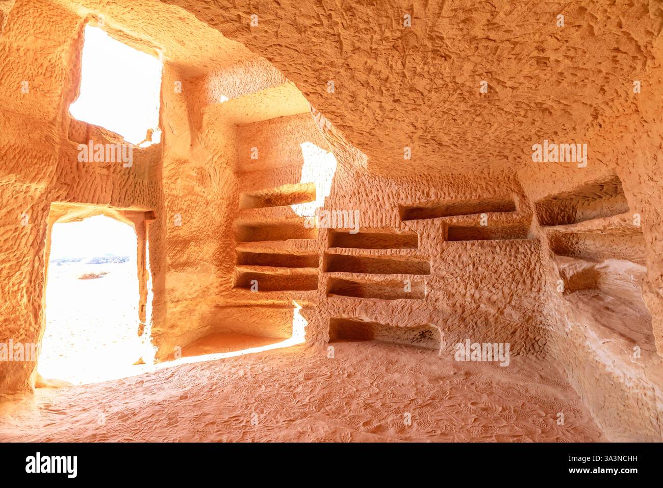 Das Sonnenlicht, das das Innere eines in Felsen gehauenen Grabes Jabal AlBanat in Hegra, Al-Ula, Saudi-Arabien, beleuchtet, offenbart komplizierte Details und alte Begräbnisse Stockfoto