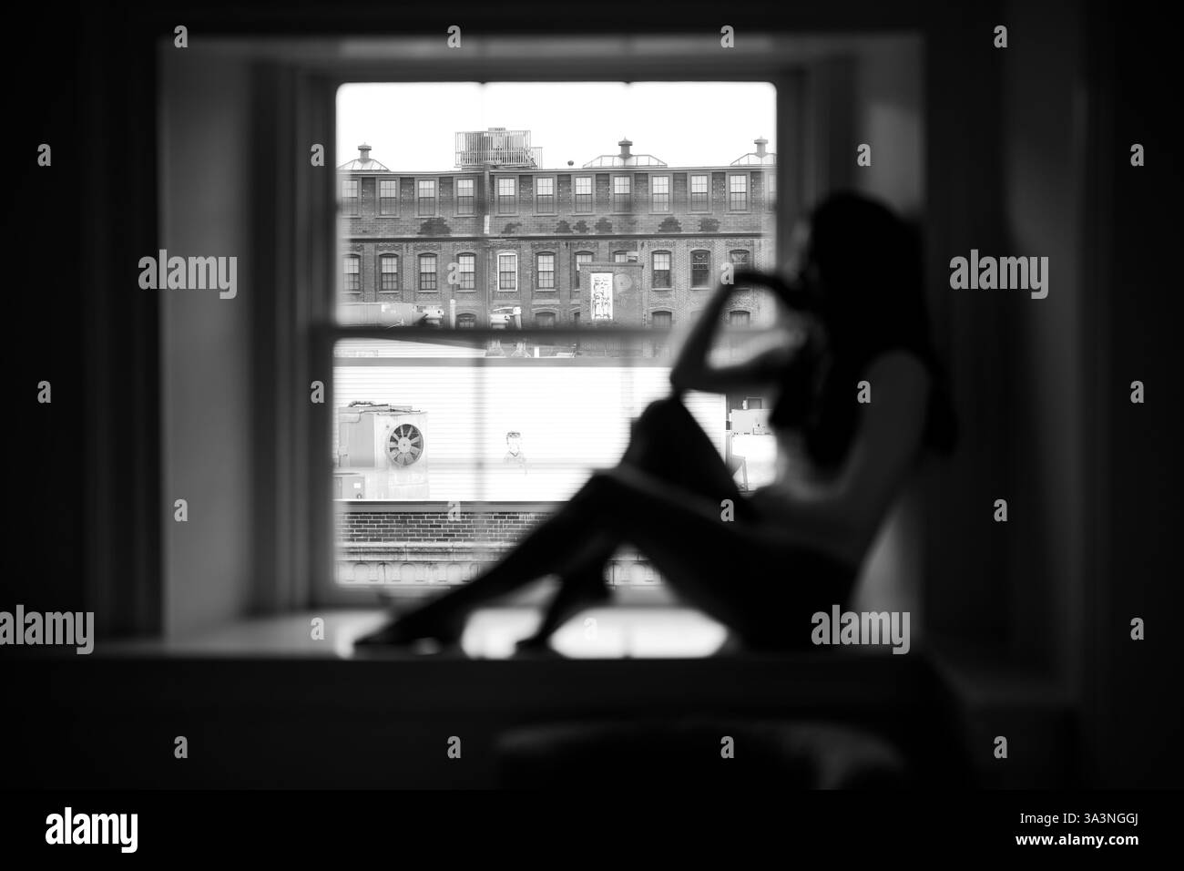 Silhouette einer Frau, die an einem Fenster sitzt, mit Blick auf städtische Gebäude Stockfoto