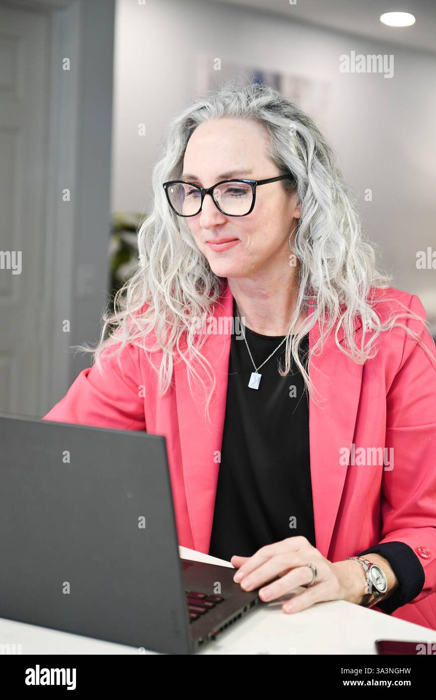 Professionelle Frau in rosa Blazer konzentriert sich auf einen Laptop in einem Werk Stockfoto