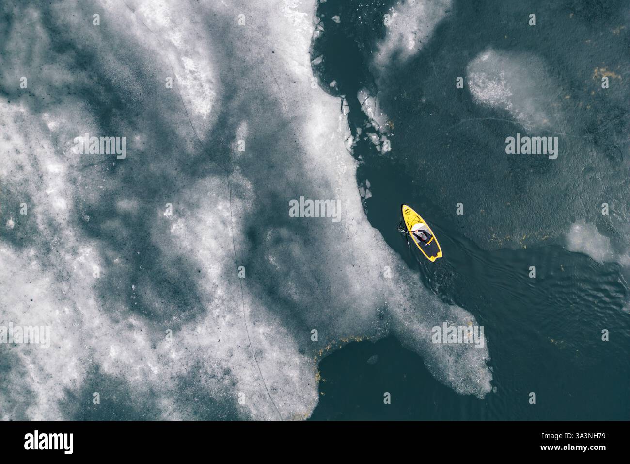 Gelbes Paddleboard (SUP), das durch eiskaltes Wasser auf einem gefrorenen See fährt Stockfoto