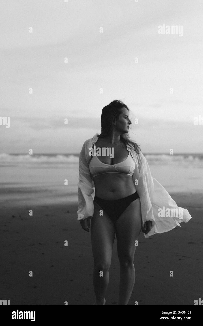 Glückliche junge Frau am Strand bei Sonnenuntergang in fließender Kleidung Stockfoto