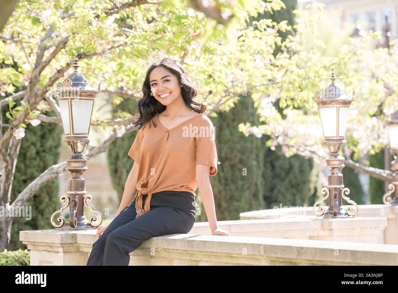 Die junge Frau sitzt auf einem Steinvorsprung und lächelt inmitten üppigen Grüns Stockfoto