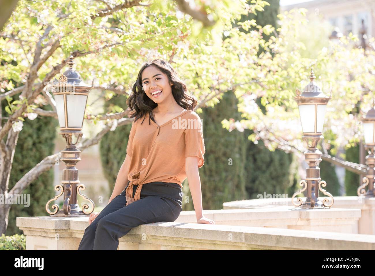 Die junge Frau sitzt lachend auf einem Steinvorsprung Stockfoto