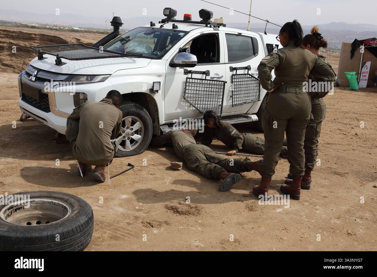 Israelische Soldaten, junge Männer und Frauen auf Patrouille in einem Pickup-Truck im Westjordanland schließen sich an, um ein Rad zu wechseln, das eine flache hatte, Jordantal Israel. Stockfoto