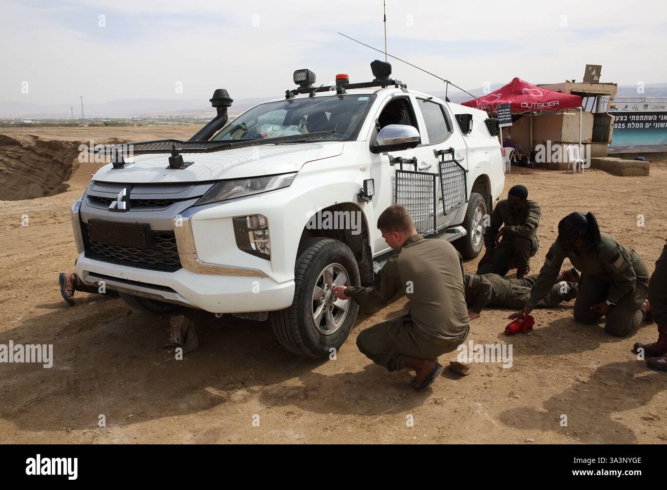 Israelische Soldaten, junge Männer und Frauen auf Patrouille in einem Pickup-Truck im Westjordanland schließen sich an, um ein Rad zu wechseln, das eine flache hatte, Jordantal Israel. Stockfoto