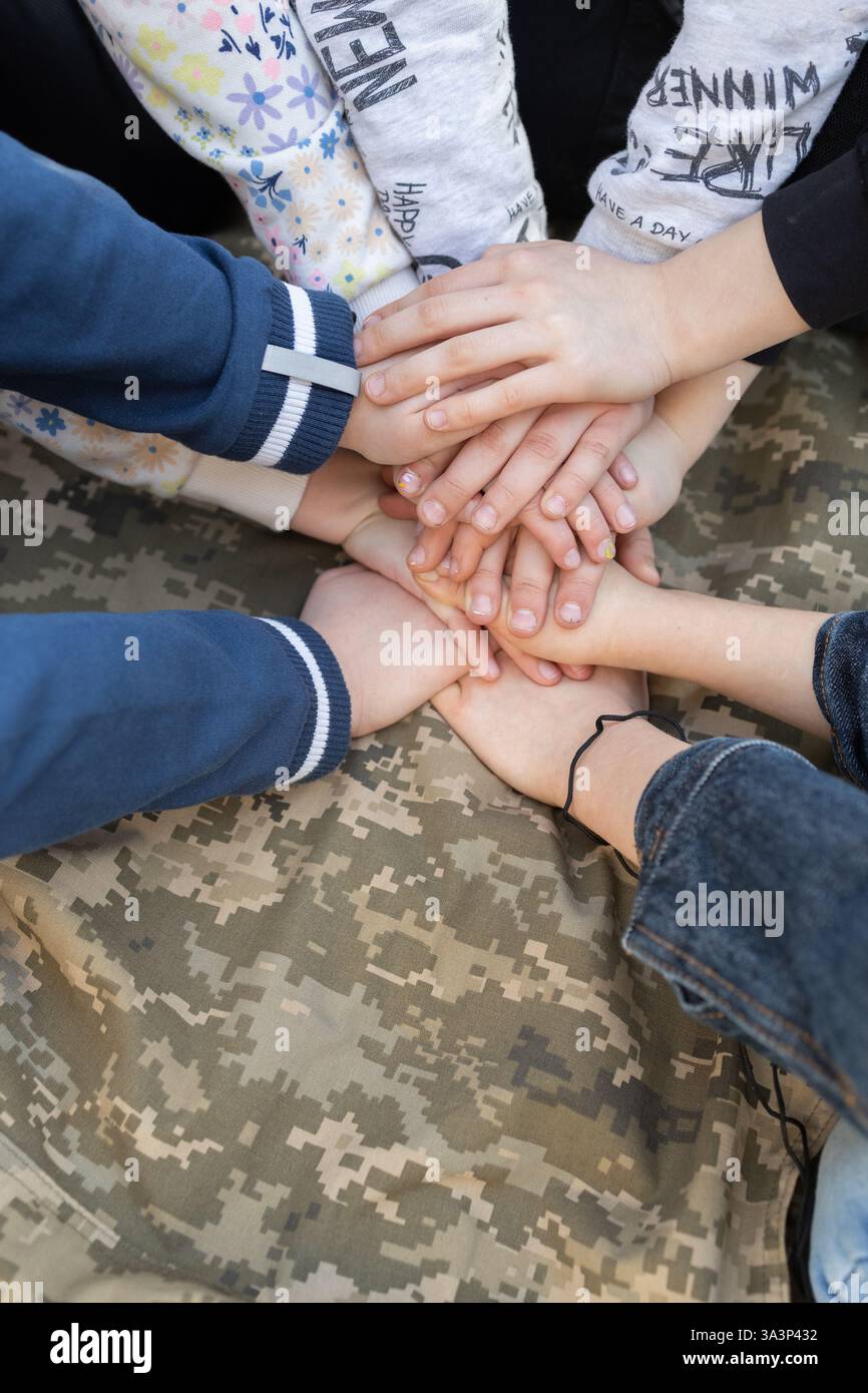Mehrere Paar Kinderhände halten sich vor dem Hintergrund einer militärischen Pixeluniform. Unterstützung der Ukraine. Tag des Verteidigers der Ukraine. Indep Stockfoto