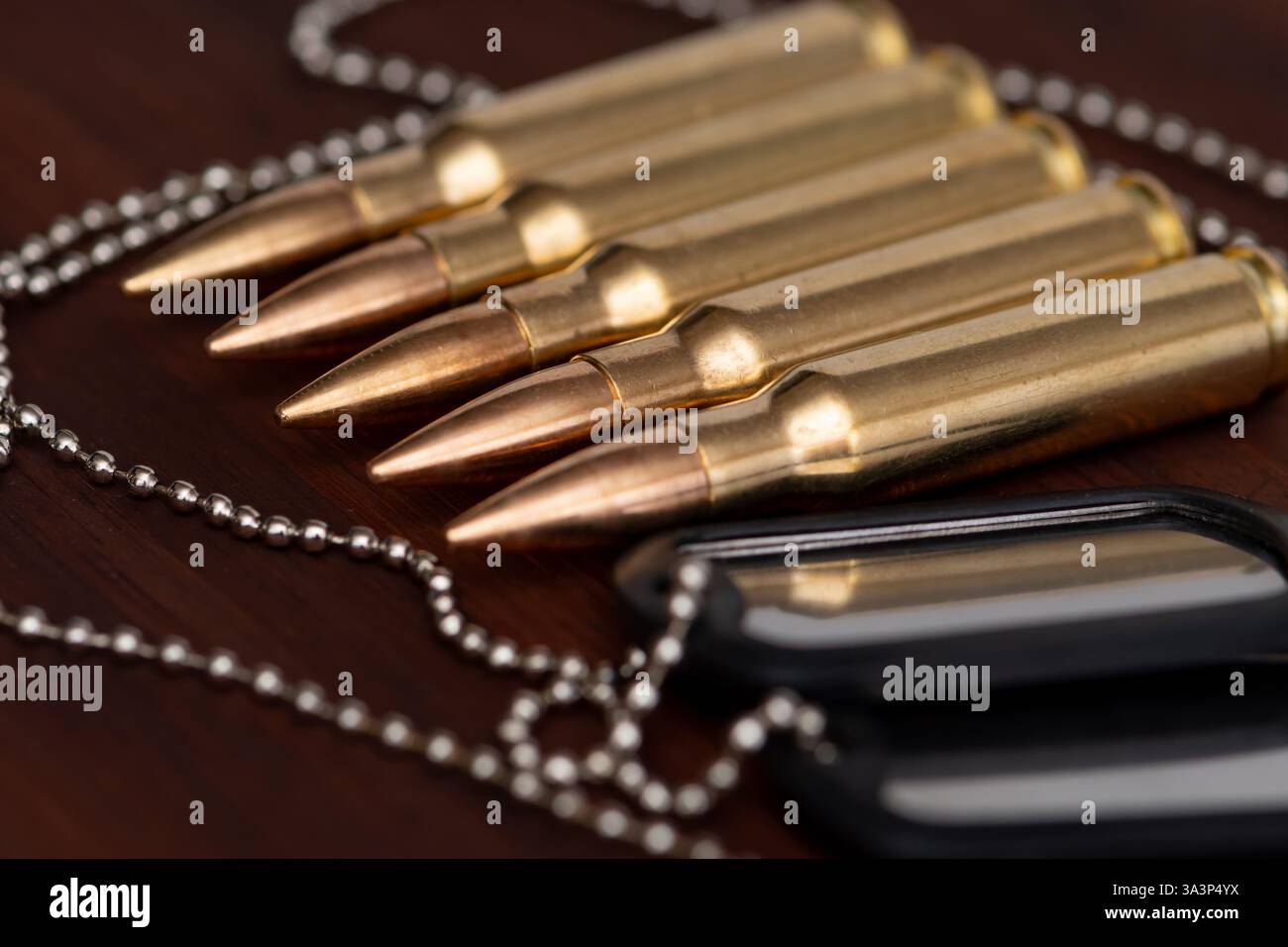 Munition und Marken - ein Symbol für den Militärdienst fünf Gewehrmunition in einer Reihe und Armeehundmarken auf einer Kette auf dunklem Hintergrund. Stockfoto