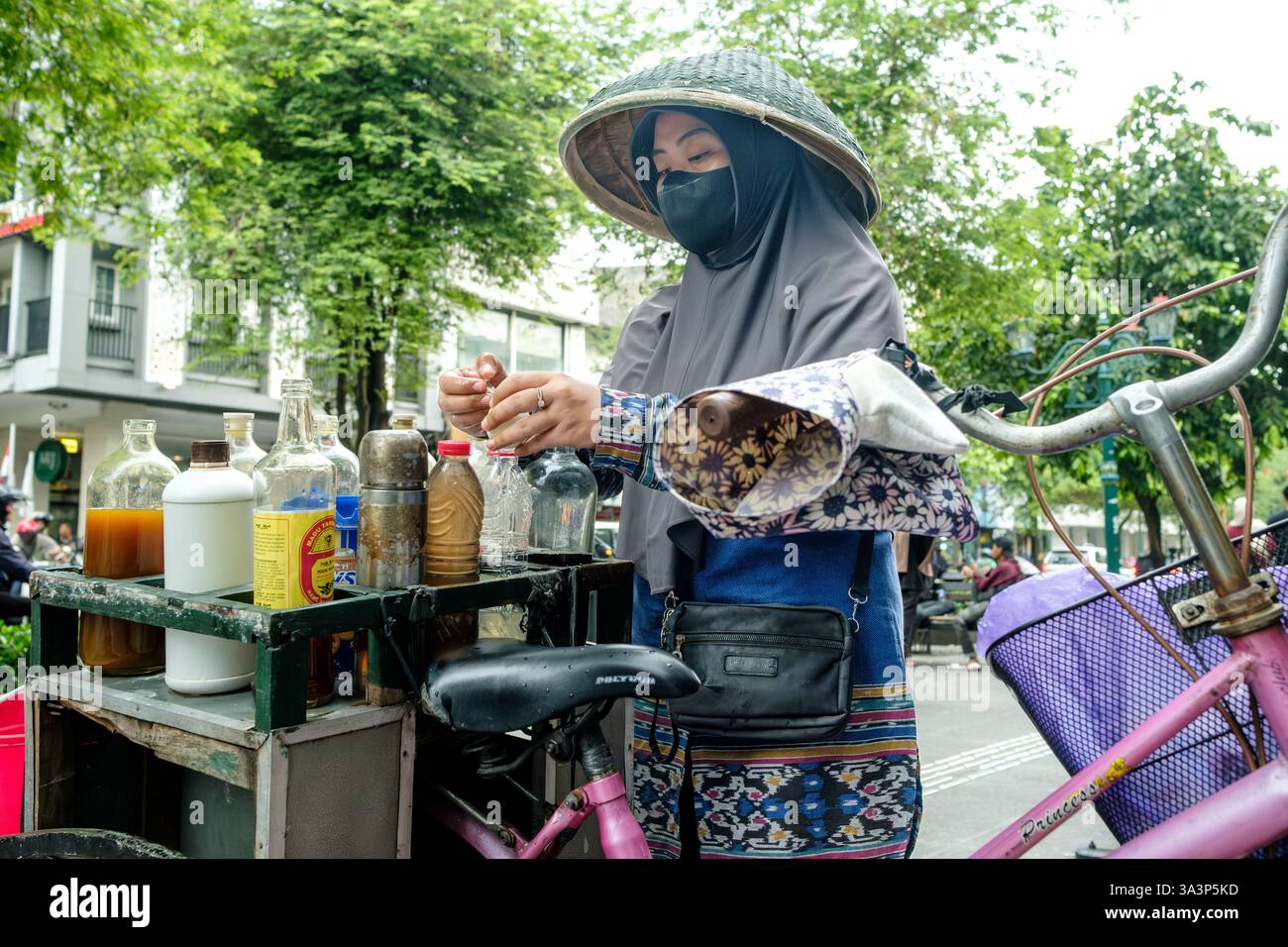 Straßenverkäufer, der Kräutermedizin auf ihrem Fahrrad in yogyakarta zubereitete, trug traditionellen Hut und Gesichtsmaske Stockfoto