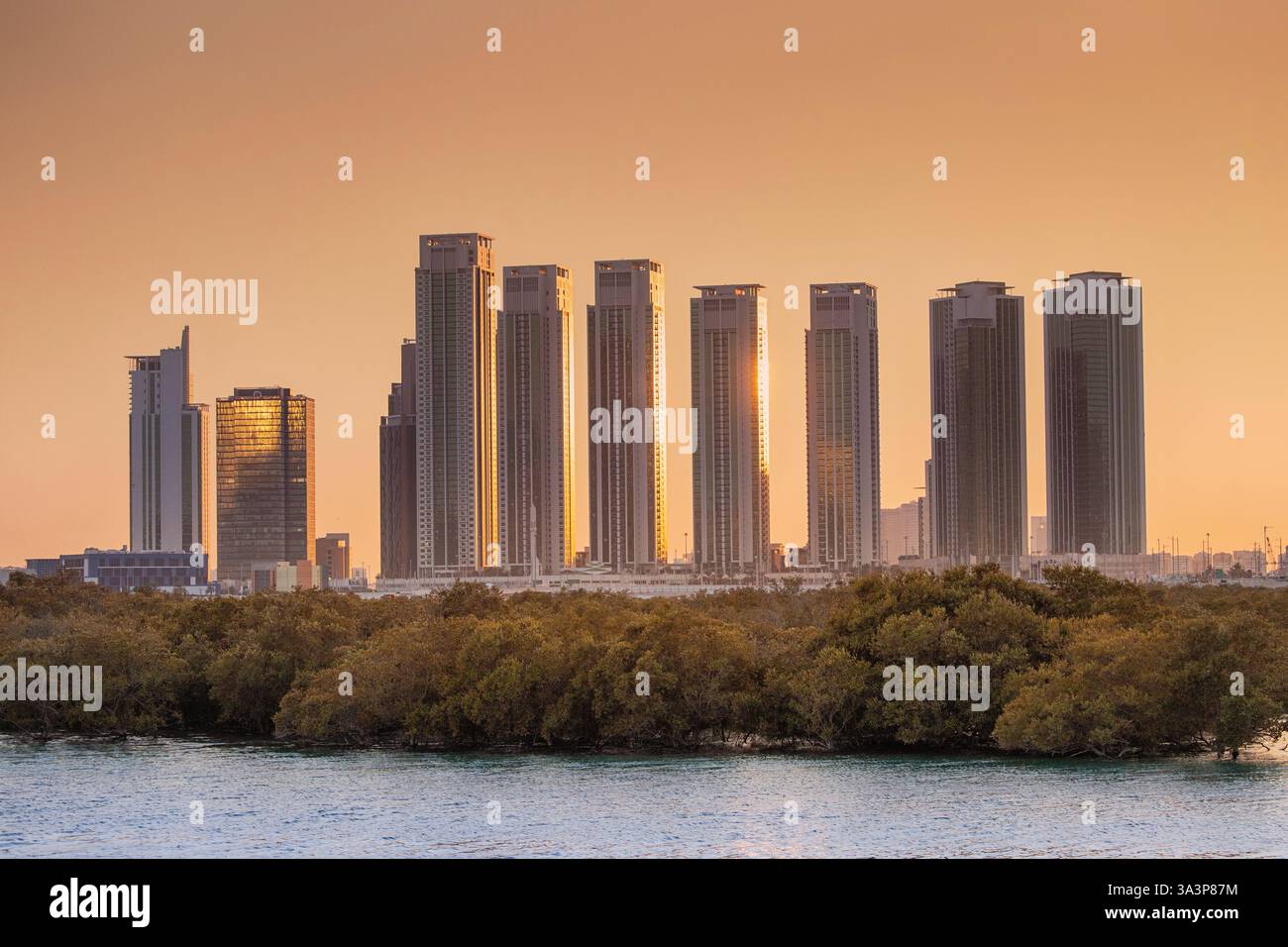 21. Januar 2025, Abu Dhabi, VAE: Panoramablick auf die Skyline von Abu Dhabi bei Sonnenuntergang mit Wolkenkratzern und Mangroven, die sich auf dem Wasser spiegeln Stockfoto