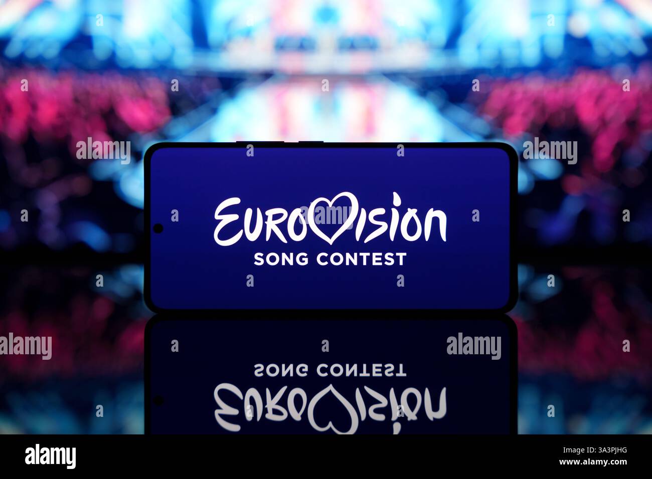 Smartphone mit Eurovision Song Contest Logo mit verschwommener Bühne und Publikum im Hintergrund. Musikwettbewerb und Unterhaltungskonzept Stockfoto