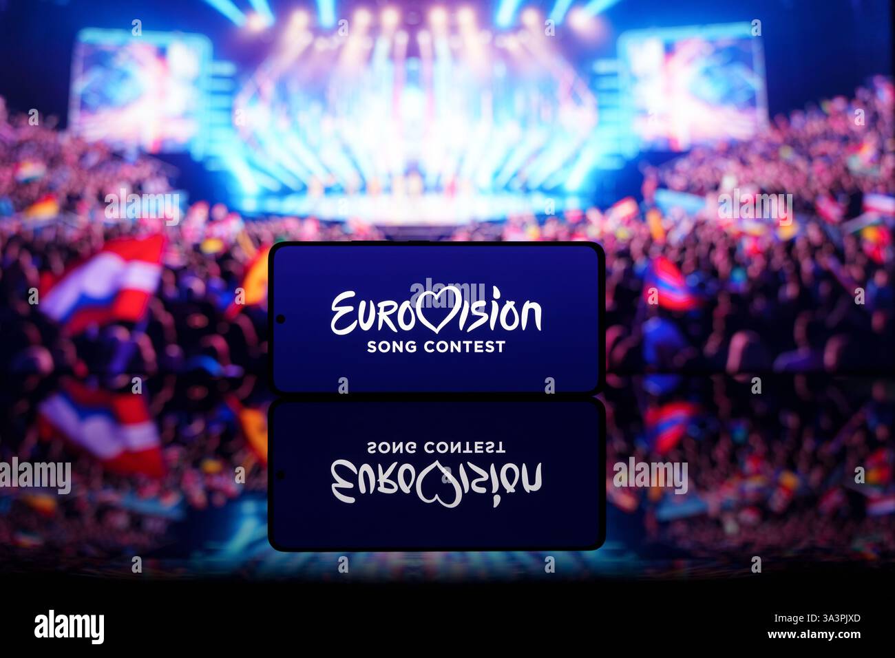 Smartphone mit Eurovision Song Contest Logo mit verschwommener Bühne und Publikum im Hintergrund. Musikwettbewerb und Unterhaltungskonzept Stockfoto