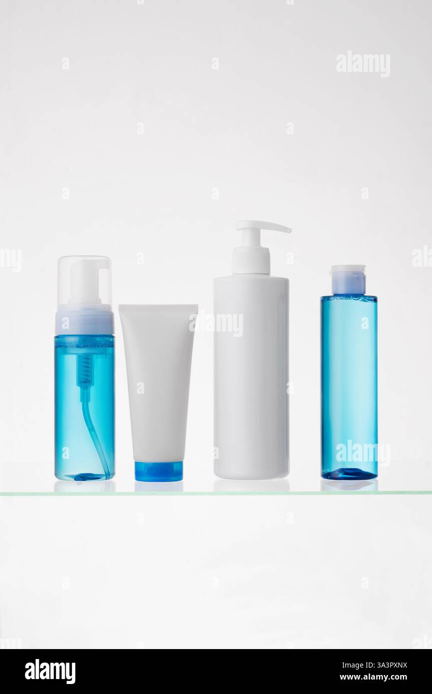 Verschiedene kosmetische Produkte auf einem Glasregal auf weißem Hintergrund. Mockup von Hautpflege- und Badeprodukten auf einem Glasregal. Spender und Röhrchen Stockfoto
